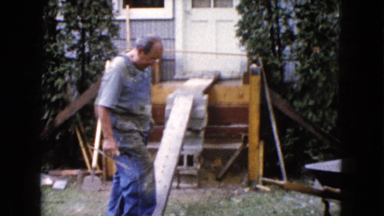 A worker in blue overalls passes the wooden ramp and unfinished deck framing in a 1960 Wauconda backyard scene.