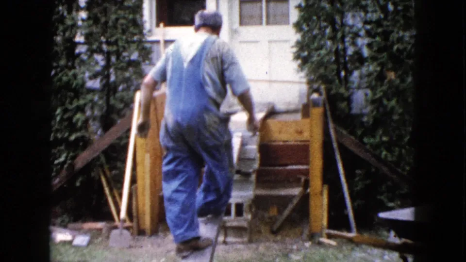 Seen from behind, the overalled worker approaches the plank ramp and unfinished backyard deck in Wauconda, Illinois, 1960.