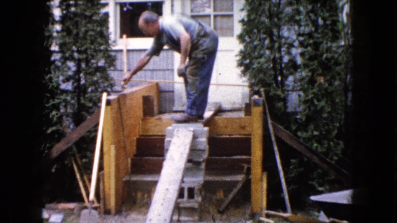 Man bends over the top of the wooden stair frame while working near the house window.