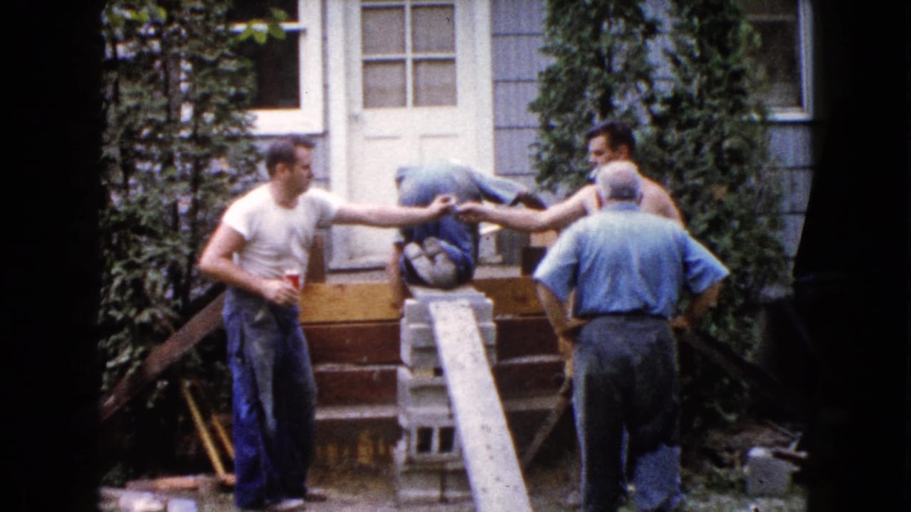 Four men outside a house entry handle a plank, cinder blocks, and tools during renovation work.