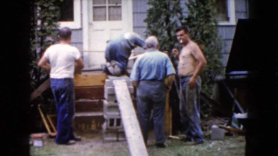 At the end of the clip, men remain around the Wauconda house entry, with tools and materials visible and one shirtless man facing the camera.