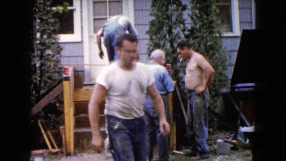 The 8mm frame shows a close foreground worker with three men behind him at a Wauconda house deck project.