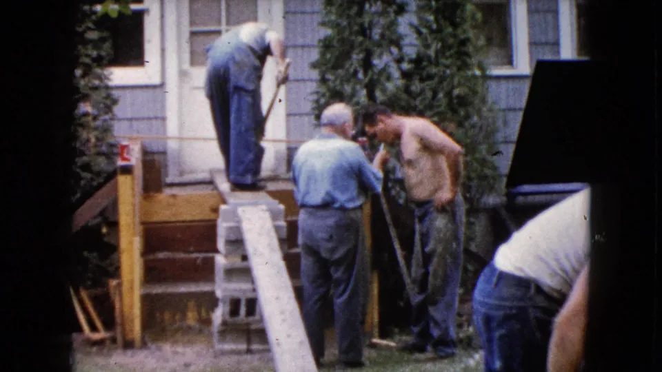 Adult men work on porch steps outside a house in Wauconda, Illinois, in 1960, with shovels, lumber, and cinder blocks visible.