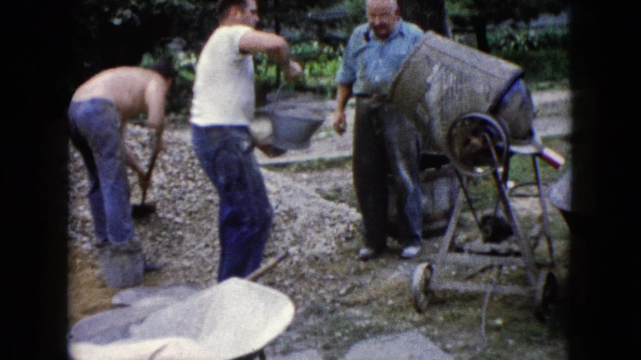 Men work with gravel and a cement mixer beside buckets and wheelbarrows in a yard.