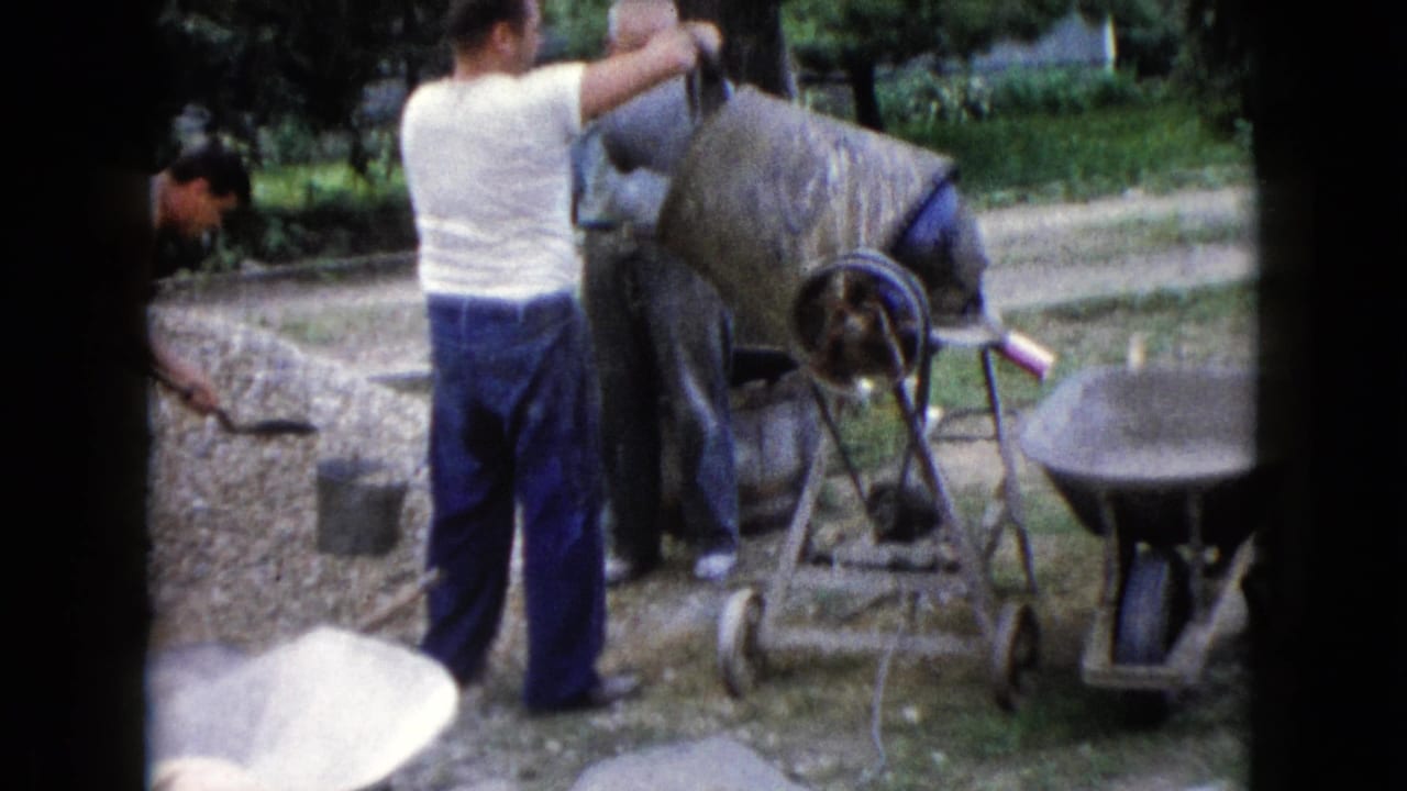 A man in a white shirt pours material into a portable cement mixer while other men work nearby in the Wauconda yard.