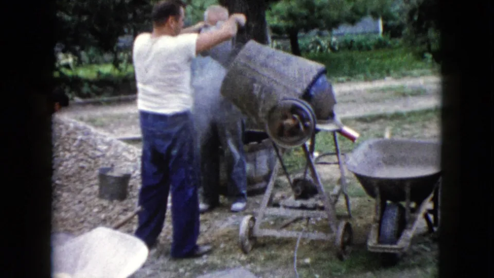 In the 1960 Wauconda home-movie scene, a man works beside the cement mixer as pale dust or mix appears around the drum.