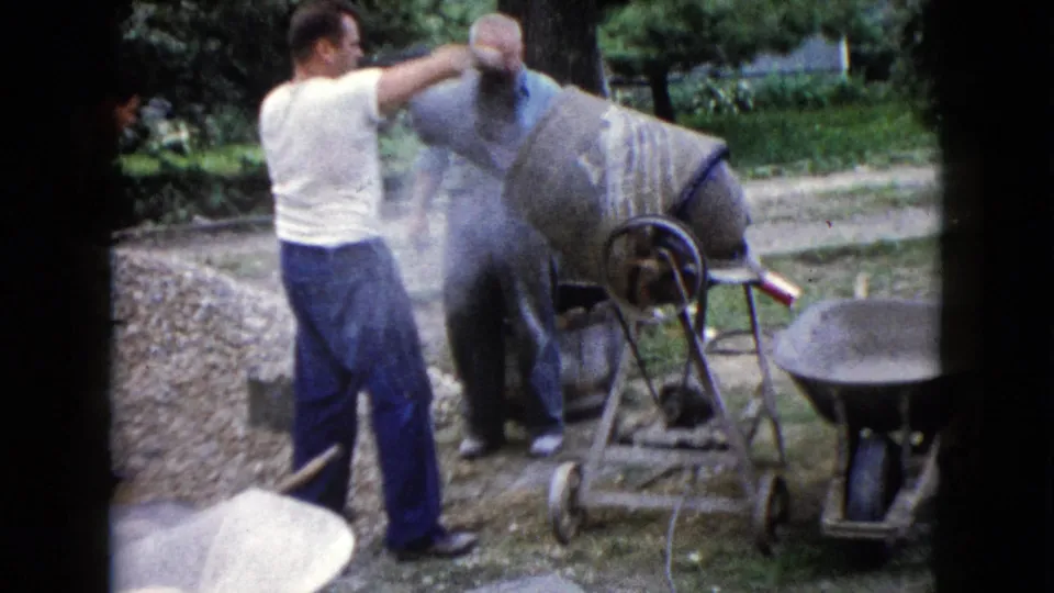 Two men continue work around the portable cement mixer in a Wauconda, Illinois yard, with wheelbarrows and buckets nearby.