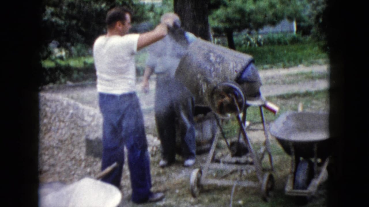 In Wauconda, Illinois, two adult men appear to work with a cement mixer near a wheelbarrow and gravel pile in 1960 home-movie footage.