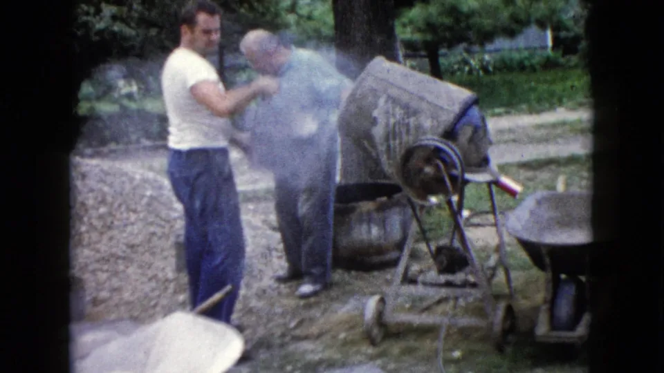 One adult man faces the camera near the cement mixer while another remains partly obscured during 1960 yard work in Wauconda, Illinois.