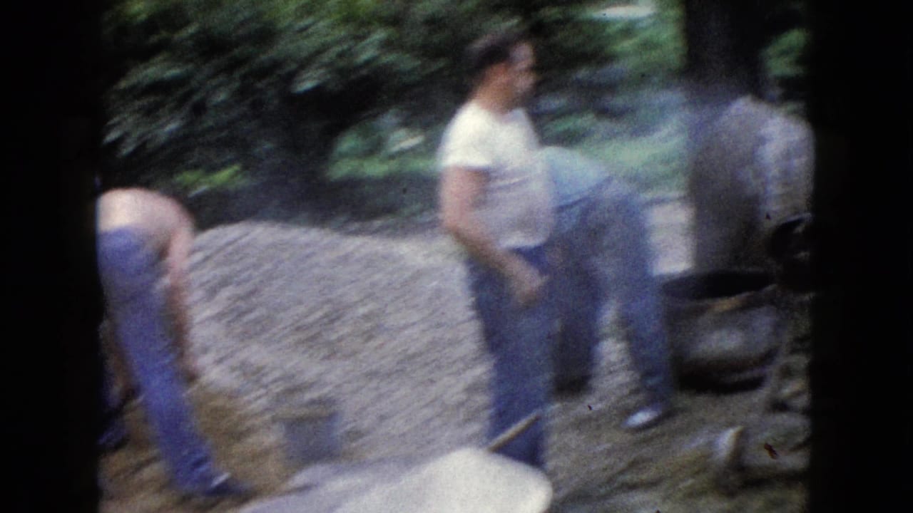 Blurred view of men near a gravel pile and cement mixer outdoors.