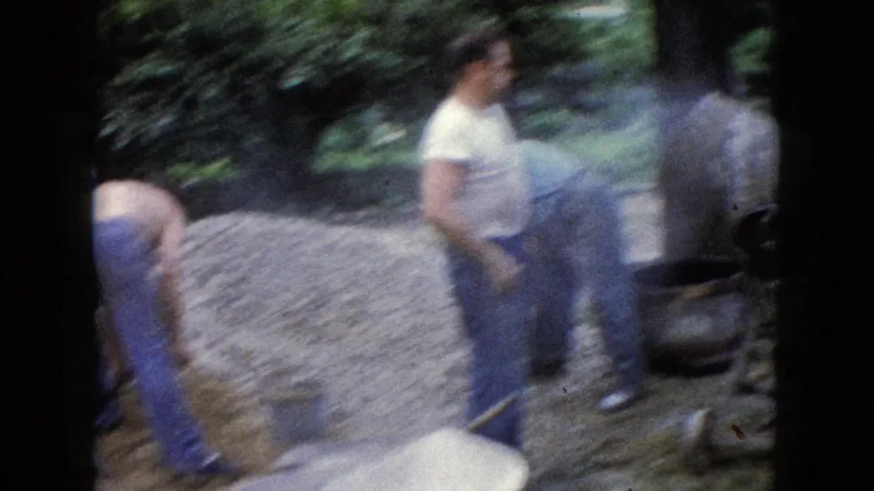 1960 8mm home-movie frame from Wauconda, Illinois, showing men moving around a gravel pile and cement mixer in a yard.