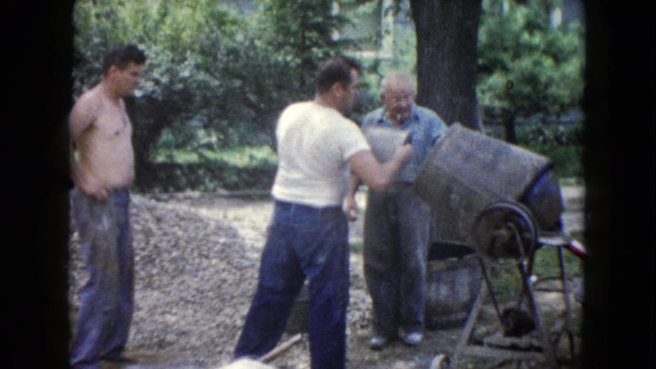 Three men stand by a cement mixer and gravel pile outdoors.