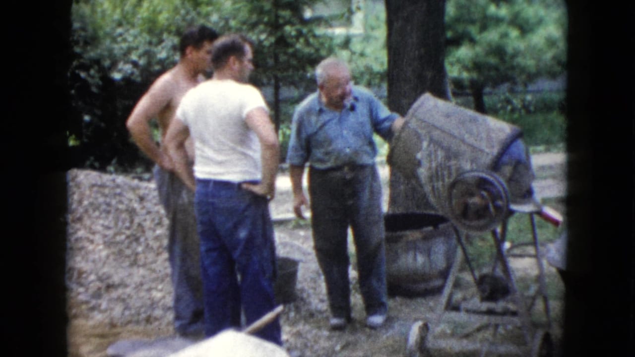 The group remains beside the mixer in the 1960 Wauconda yard, with the older man facing the equipment and the younger men watching.