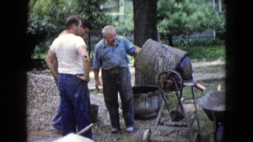 The older man in a blue shirt stands near the mixer, with two younger men nearby in the Wauconda, Illinois home-movie scene.