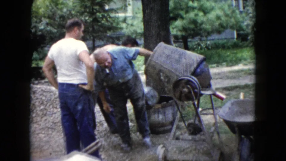 At the end of the clip, the older man bends toward the ground near the mixer while the younger men stand close in the 1960 Wauconda yard.