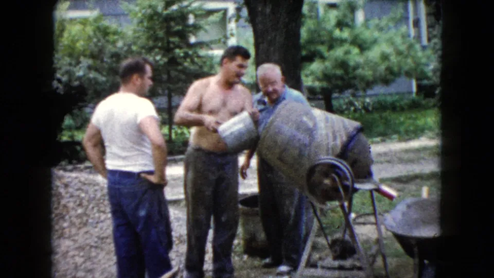 The shirtless man holds a metal bucket as the group works around the cement mixer in the 1960 Wauconda yard scene.
