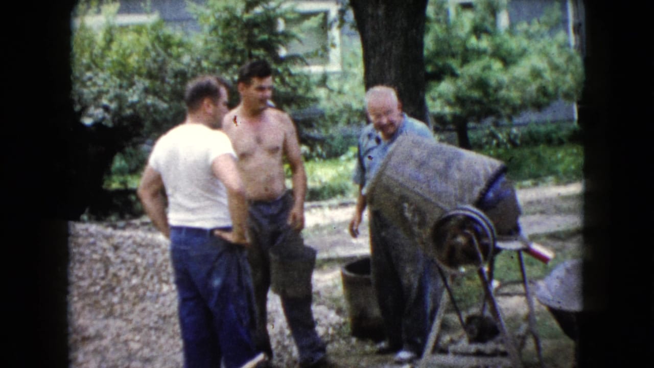 Three adult men stand near a concrete mixer in a backyard work area.