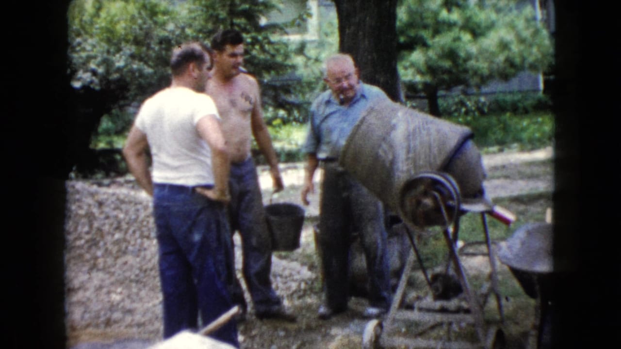 Three men stand around a concrete mixer, with one holding a bucket.