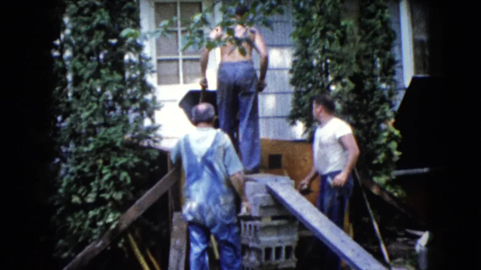 In this Wauconda 1960 frame, one man stands near the wheelbarrow at the top of the ramp while two men remain below by the blocks.