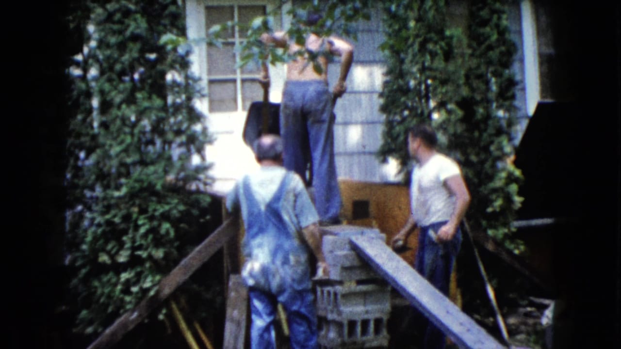 In 1960 Wauconda, Illinois home-movie footage, three adult men work near an ivy-covered house wall with planks and cinder blocks.