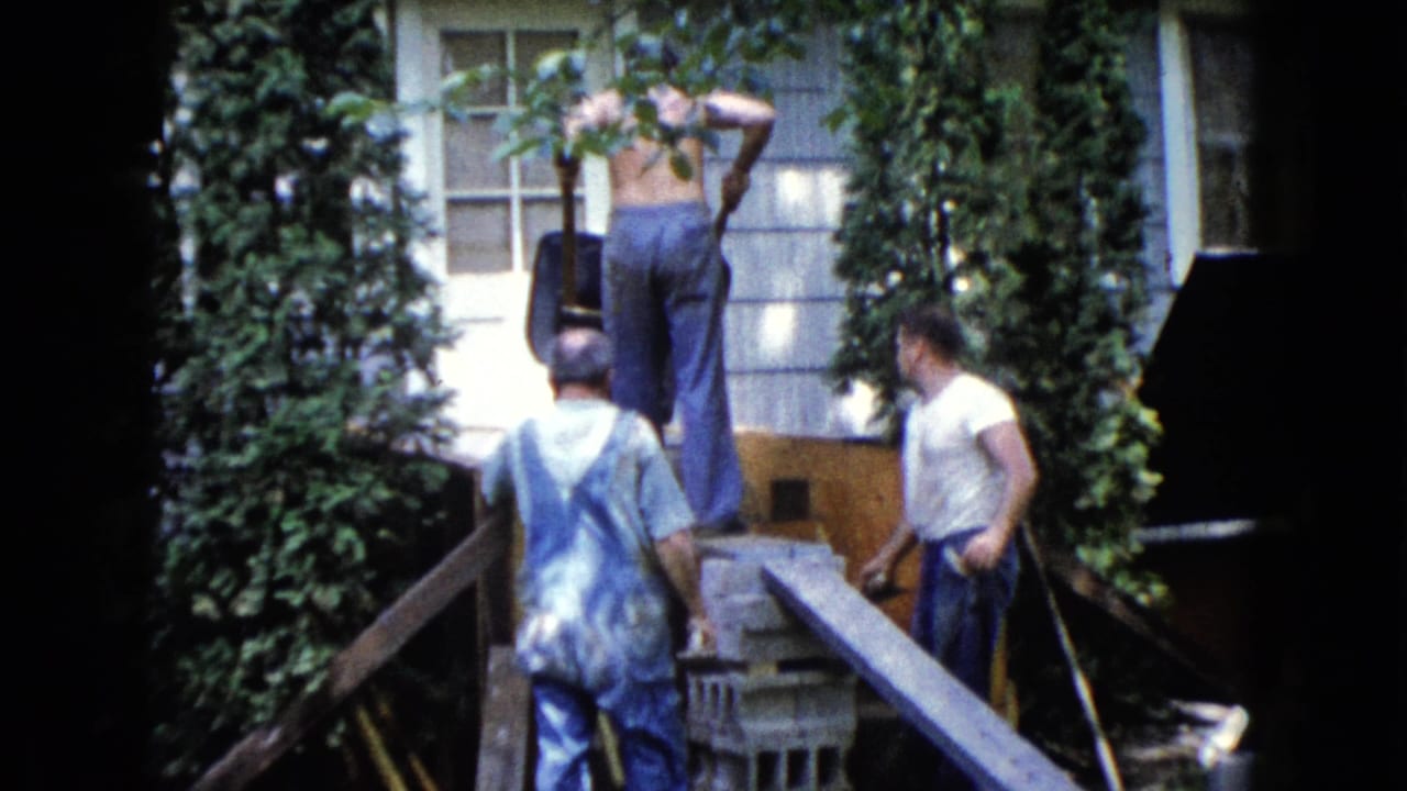 Three men continue exterior house work in Wauconda, Illinois, with one shirtless man elevated near the wall and two others below.