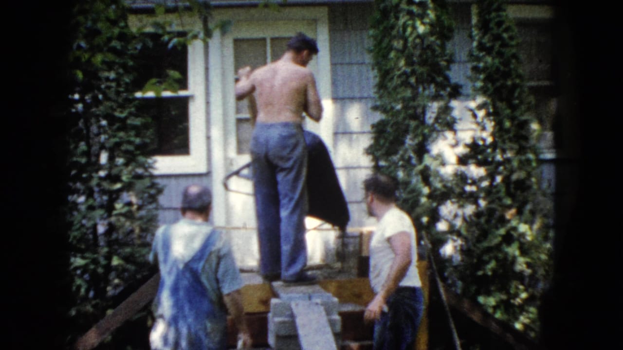 Men continue exterior house repair in Wauconda, Illinois, with ivy, light siding, and makeshift planks visible in the frame.