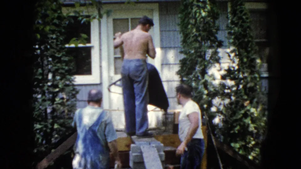 Men continue exterior house repair in Wauconda, Illinois, with ivy, light siding, and makeshift planks visible in the frame.