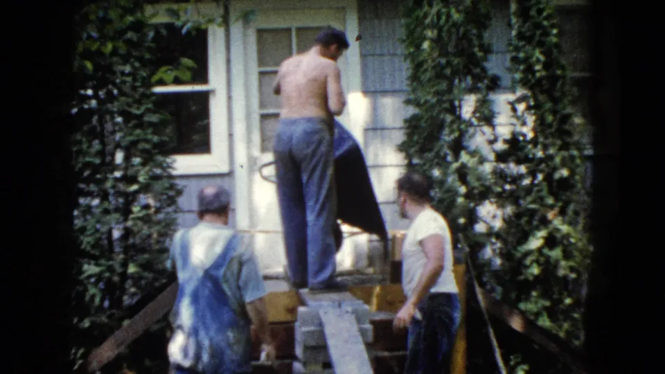 Home-movie view of a small group working near a window and ivy-covered siding during a 1960 house renovation in Wauconda.