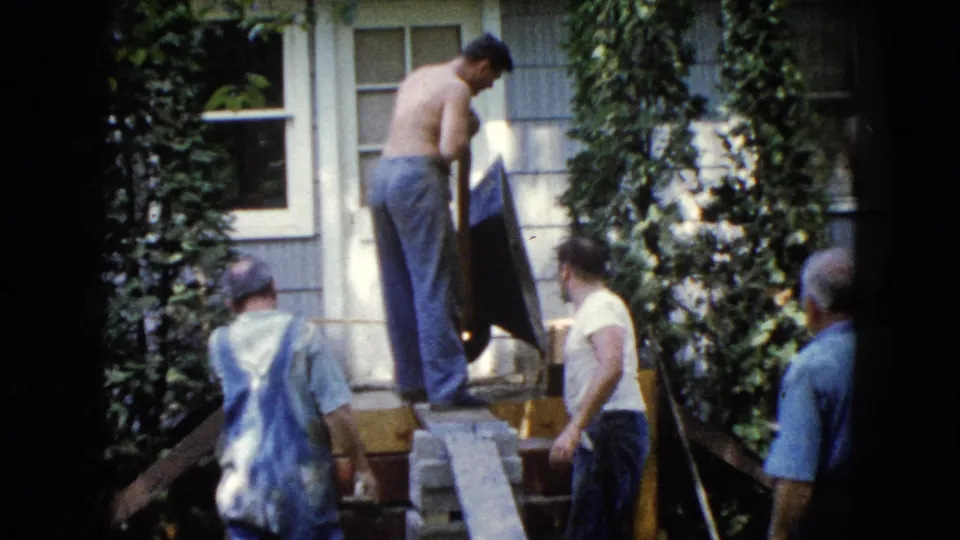 Four men are visible around an exterior repair setup at an ivy-covered Wauconda house, with boards, steps, and siding in view.