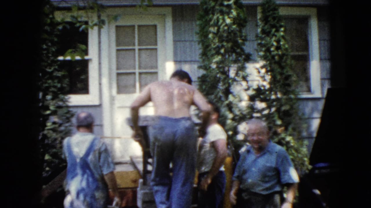 A shirtless man stands near the ramp while other men gather beside the house.