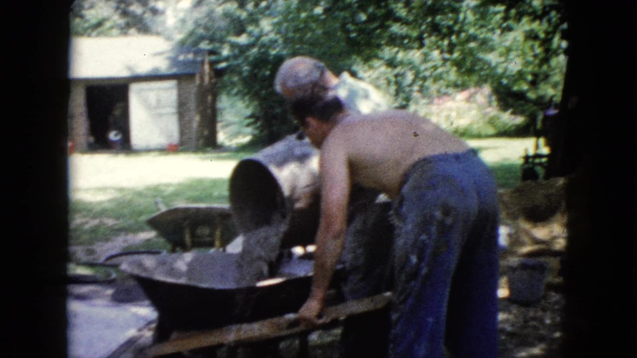 A shirtless man in blue pants tips a barrel into a wheelbarrow during 1960 backyard work in Wauconda, Illinois.