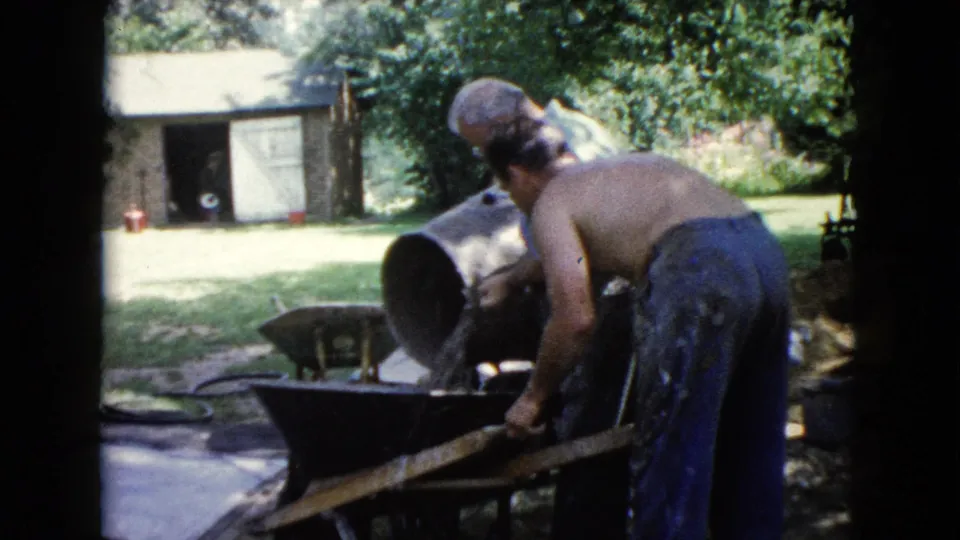 The backyard work continues as a man bends over a wheelbarrow beside a tipped barrel in Wauconda, Illinois, 1960.