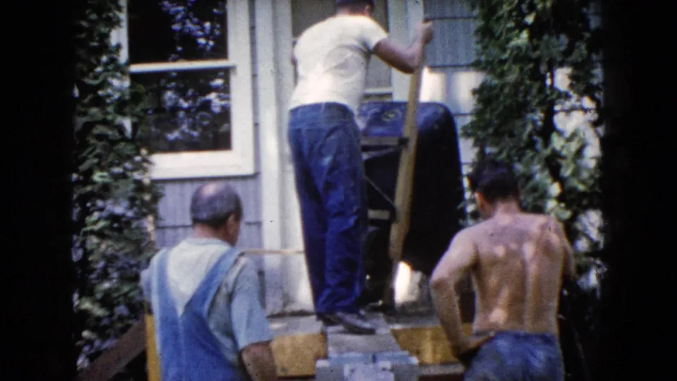 The 8mm frame shows a residential work scene in Wauconda, Illinois, with men, wood planks, siding, and a wheelbarrow.