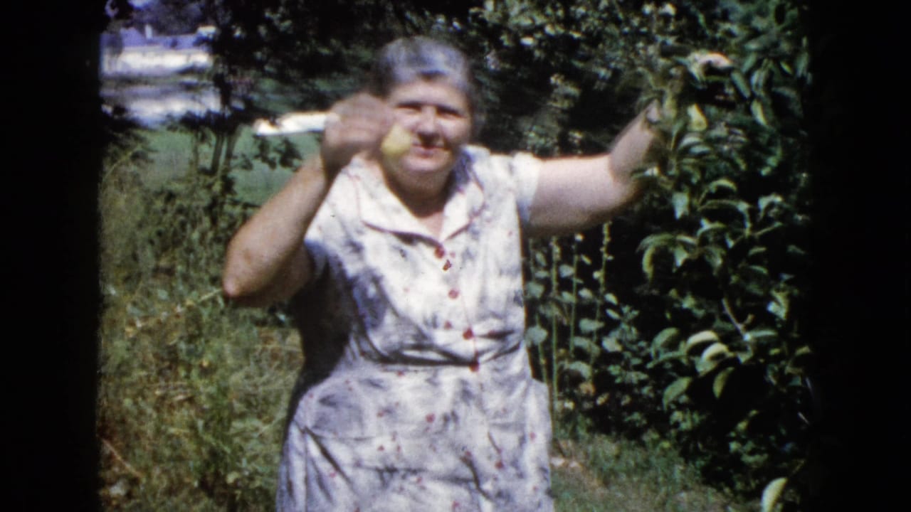 Older woman in a floral dress holds yellow fruit beside leafy branches in a sunny garden.