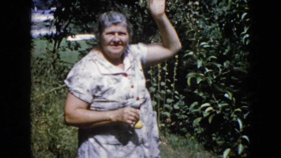 In a Wauconda garden, the woman faces the camera with fruit in one hand and her other arm raised beside the tree.