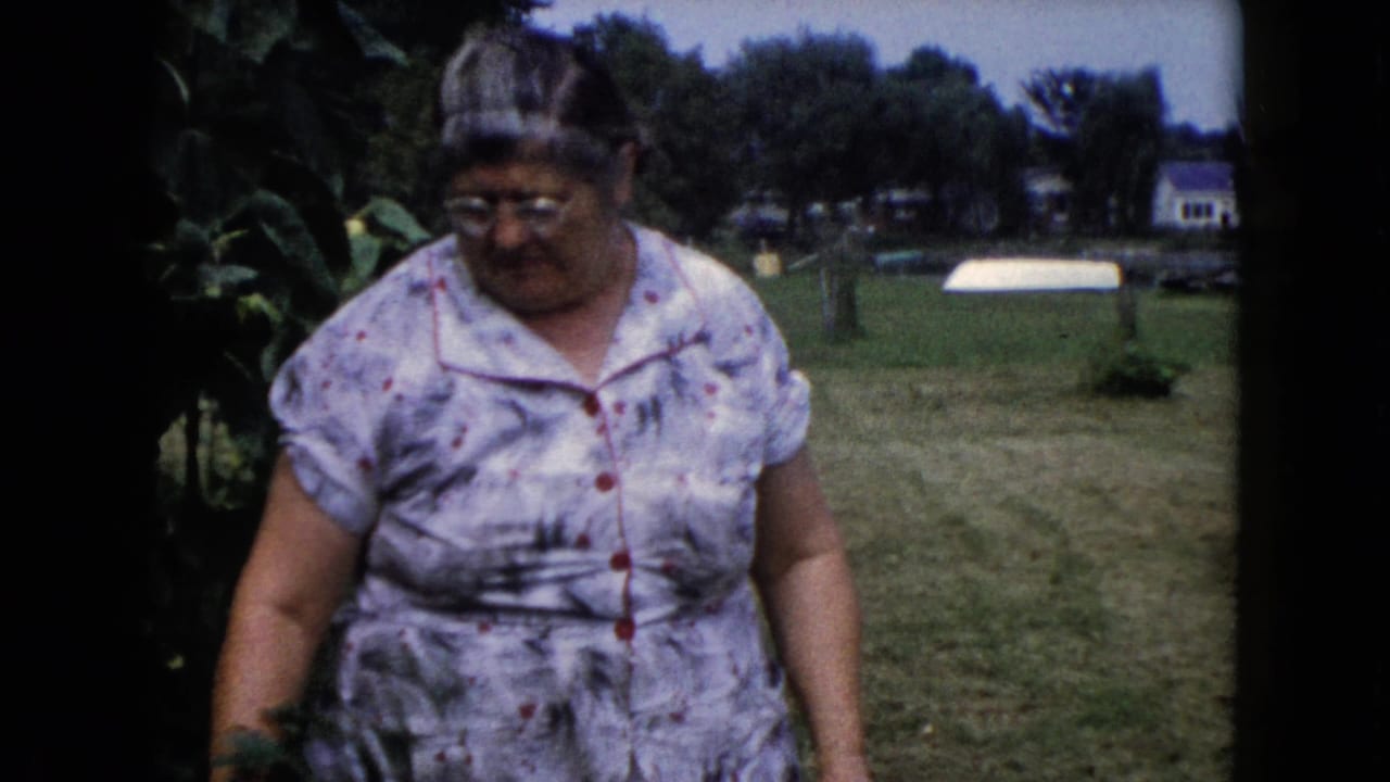 In Wauconda, Illinois home-movie footage from 1960, an older woman in a floral dress stands near garden foliage in a backyard.