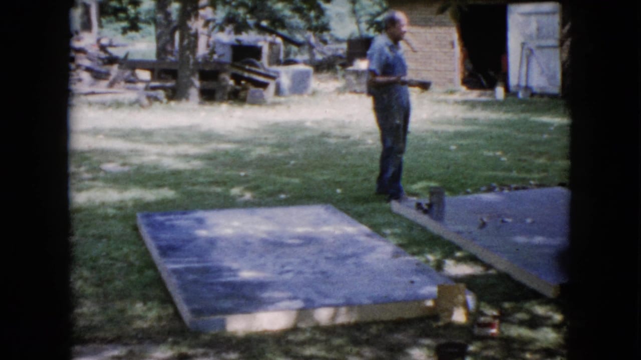 In Wauconda, Illinois, 1960, a man stands in a backyard near two concrete slabs, holding a measuring tool or tape.