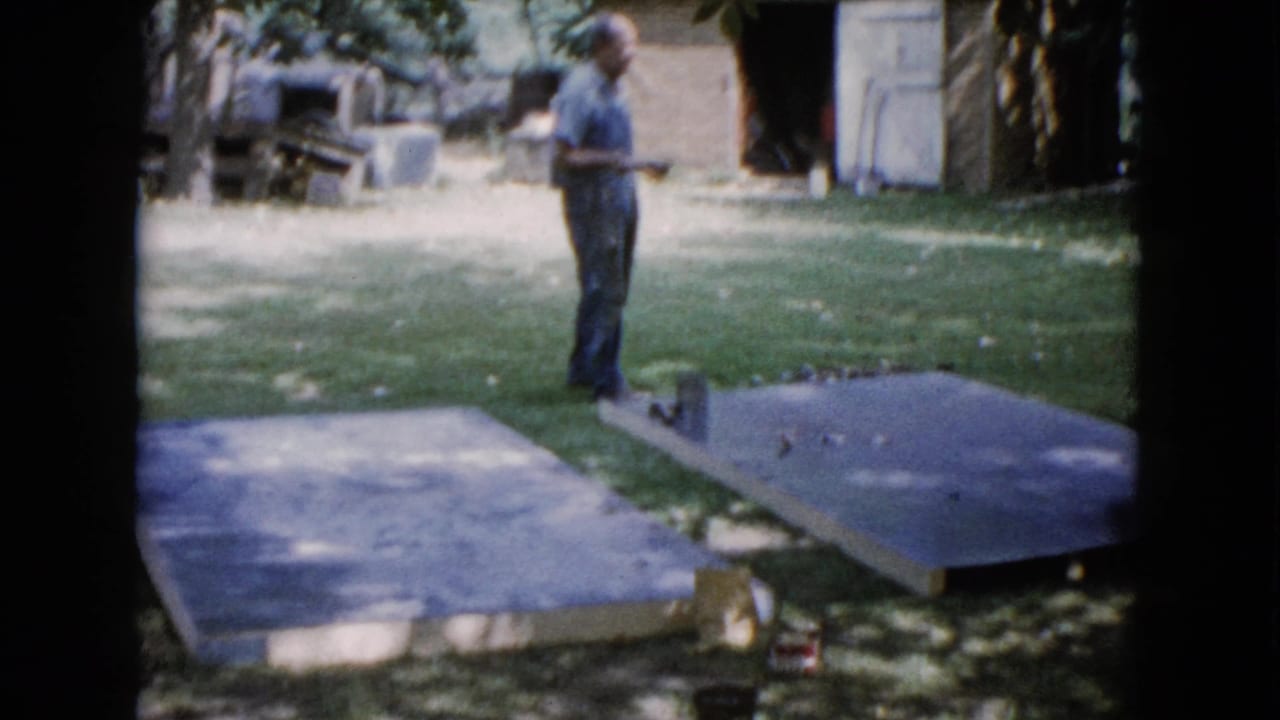 The man remains near the slabs in the 1960 Wauconda backyard, with trees and a brick outbuilding behind him.