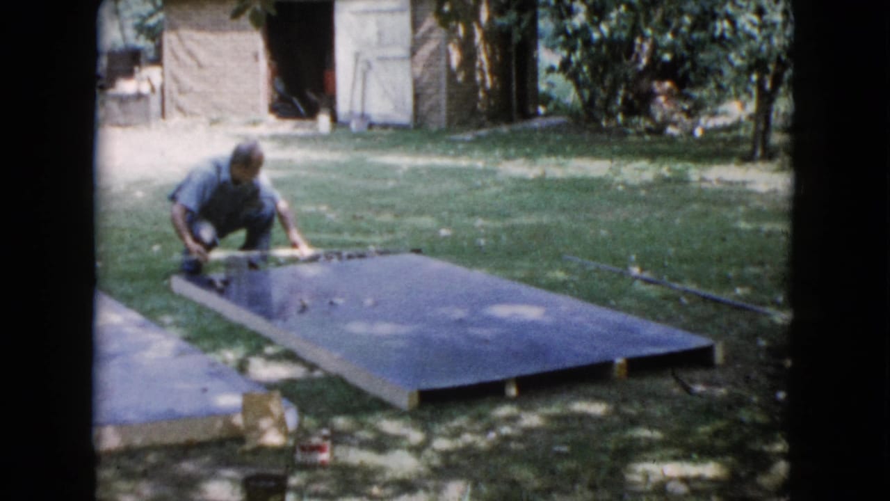 Man kneels beside a large slab in a grassy backyard near a shed.