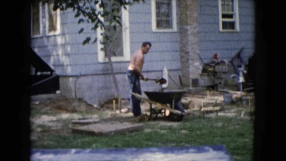A shirtless man appears to shovel or position dirt by a wheelbarrow in the Wauconda backyard work area.