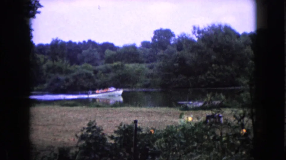 A small boat is visible on the calm lake in Wauconda, Illinois, with grass, shrubs, and trees around the shore.