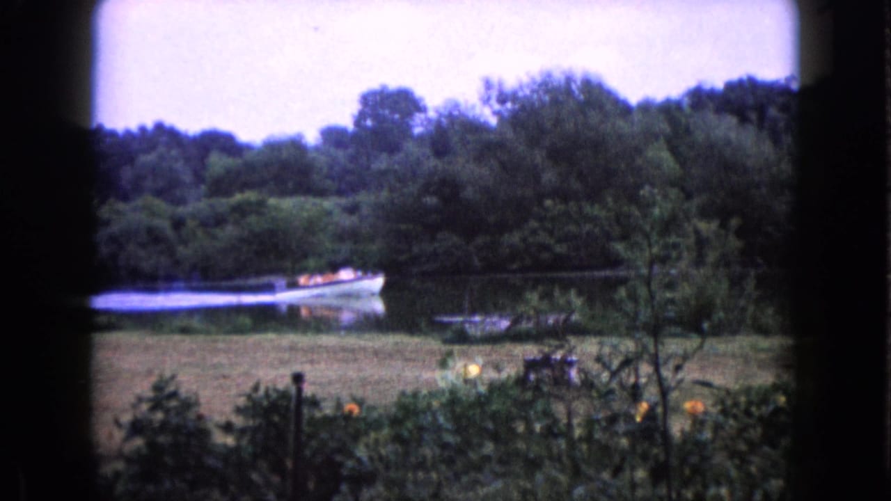 Small boat carrying people, some in bright life jackets, passes along a wooded lake in Wauconda, Illinois in 1960 footage.