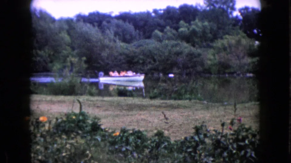 1960 home-movie view of a small boat carrying seated passengers in life jackets across a calm Wauconda lake.