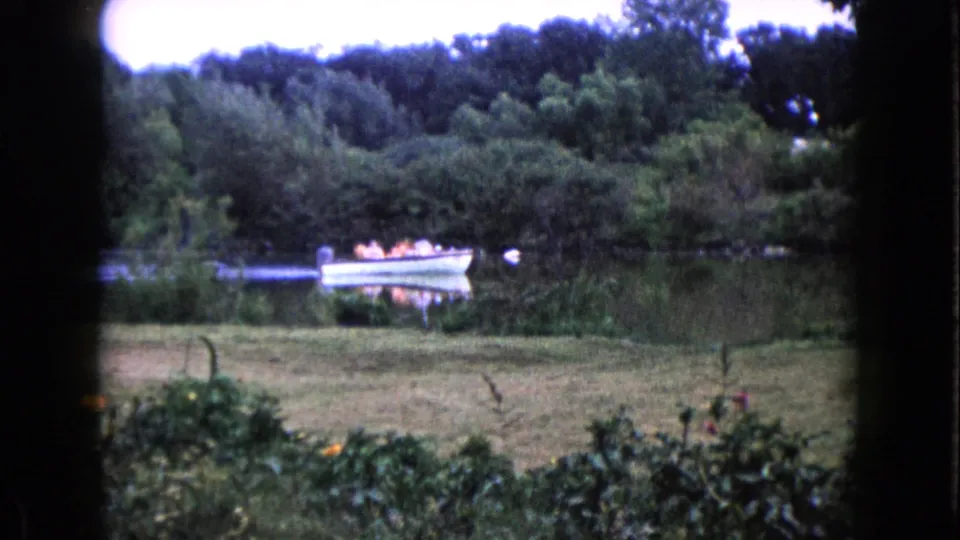 Wauconda, Illinois 1960 frame with a small boat of passengers near the far shore, seen through dark 8mm frame edges.