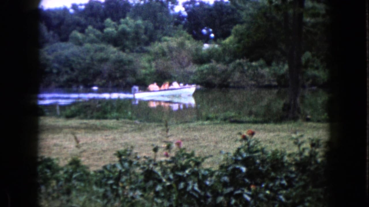 The boat moves farther along the Wauconda river scene, with passengers visible and dense green trees behind the water.