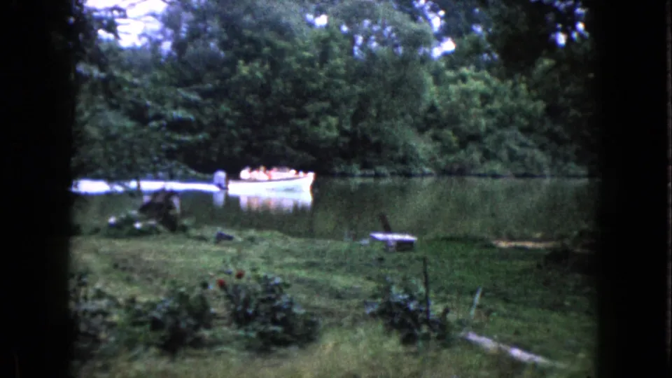 By the final frame, the small white motorboat has moved along the Wauconda river past dense trees and a grassy shore.