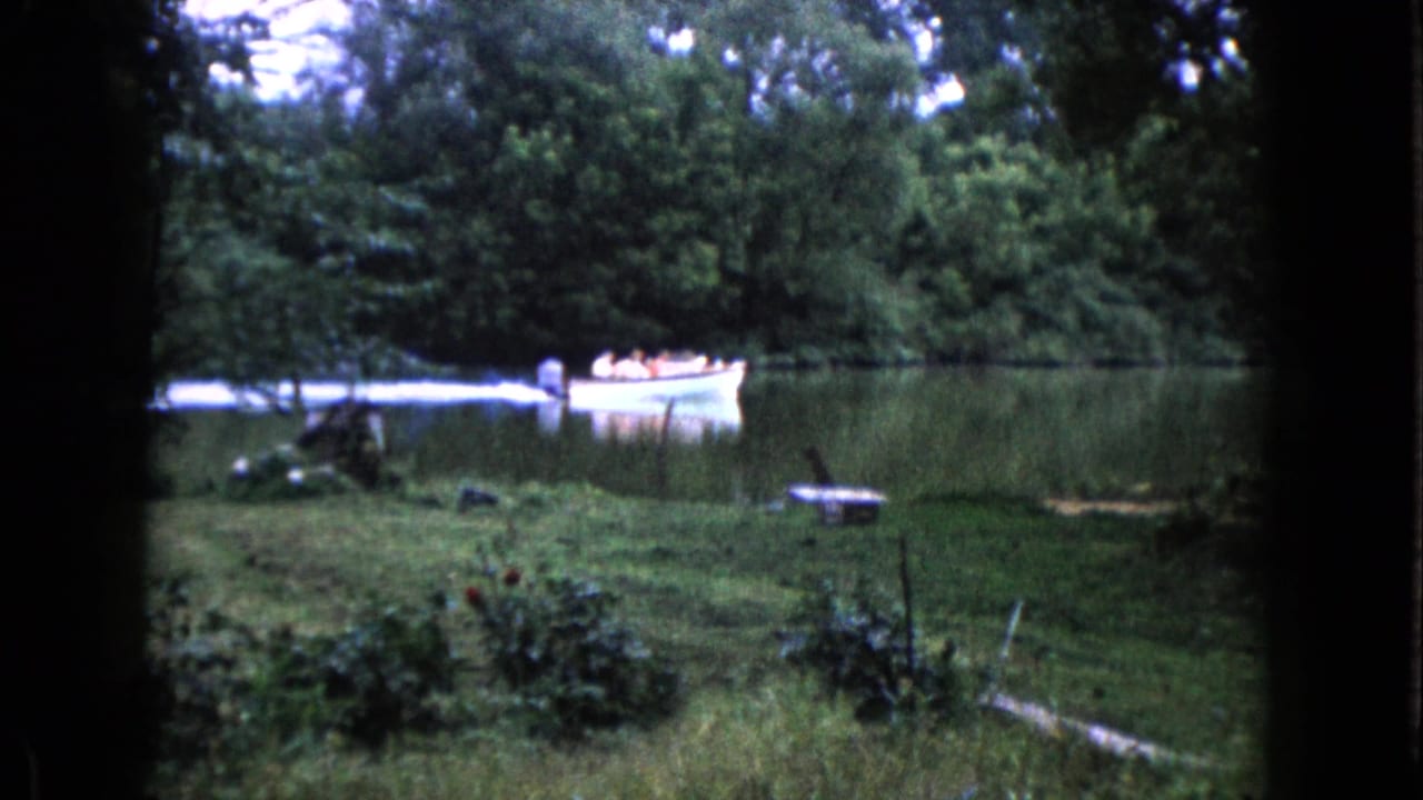 Small motorboat with passengers crossing a calm lake near a grassy shore and trees.