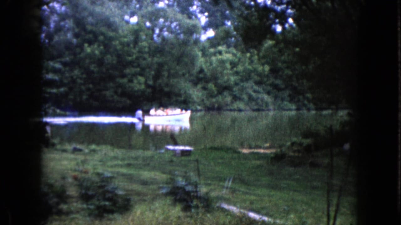 A small boat carrying people moves across a wooded Wauconda lake in 1960 home-movie footage.