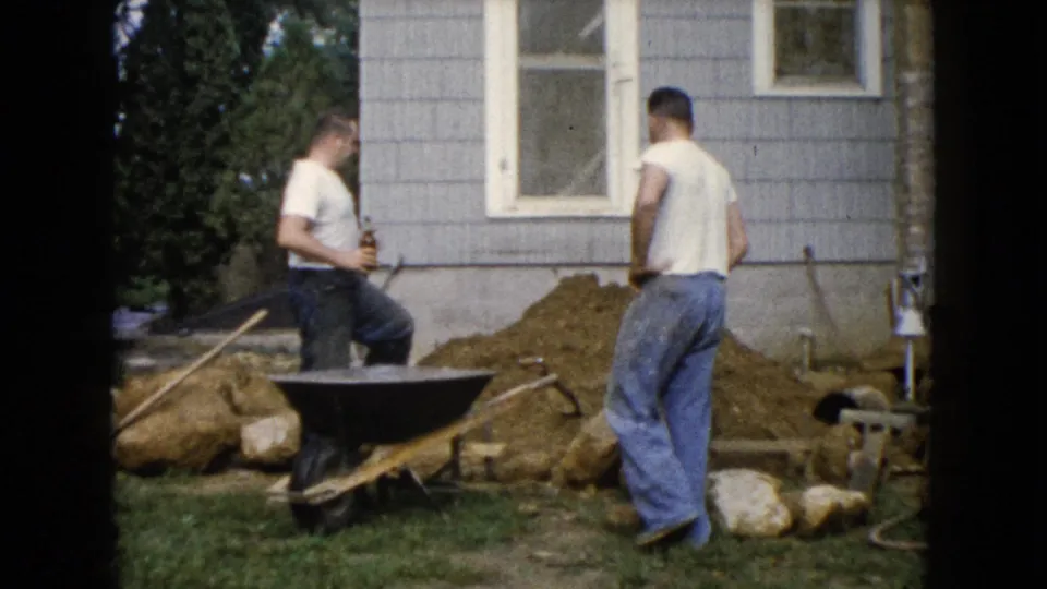 In Wauconda, Illinois, 1960, one man holds a bottle while another stands by a dirt pile near a house.
