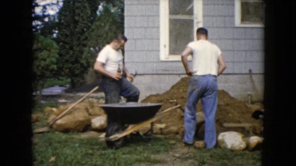 In Wauconda, Illinois, 1960, two men remain beside the wheelbarrow and landscaping materials outside a house.